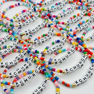 May include: A collection of elastic bracelets made from multicolored glass beads and white square plastic beads. Each bracelet features the text X CHURCH printed in black on the white beads, accented with small gold-toned metal spacer beads.