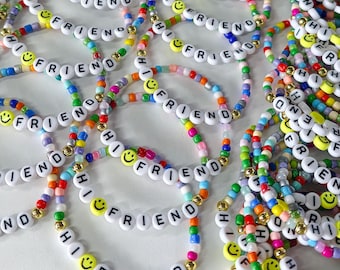 May include: A collection of colorful beaded bracelets featuring white letter beads that spell out HI FRIEND, interspersed with yellow smiley face beads and small metallic gold spacer beads. The bracelets are made from various multi-colored glass beads.