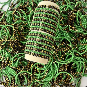 May include: A collection of elastic bracelets featuring alternating rows of bright green seed beads and black circular beads with the gold-colored text IRON DIAMOND printed on them, stacked on a cylindrical display stand.