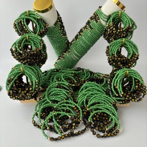 May include: A collection of beaded bracelets arranged on a display stand. The bracelets feature alternating sections of small green glass beads and black circular beads with gold lettering that spells out the word DIAMOND, accented by tiny gold beads.