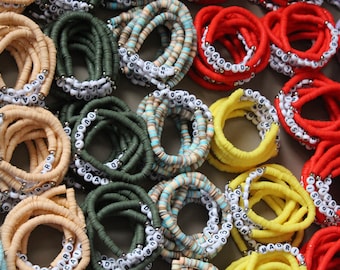 May include: Assortment of colorful beaded bracelets with white letter beads spelling out different words. The bracelets are made of various materials, including rubber, plastic, and fabric.