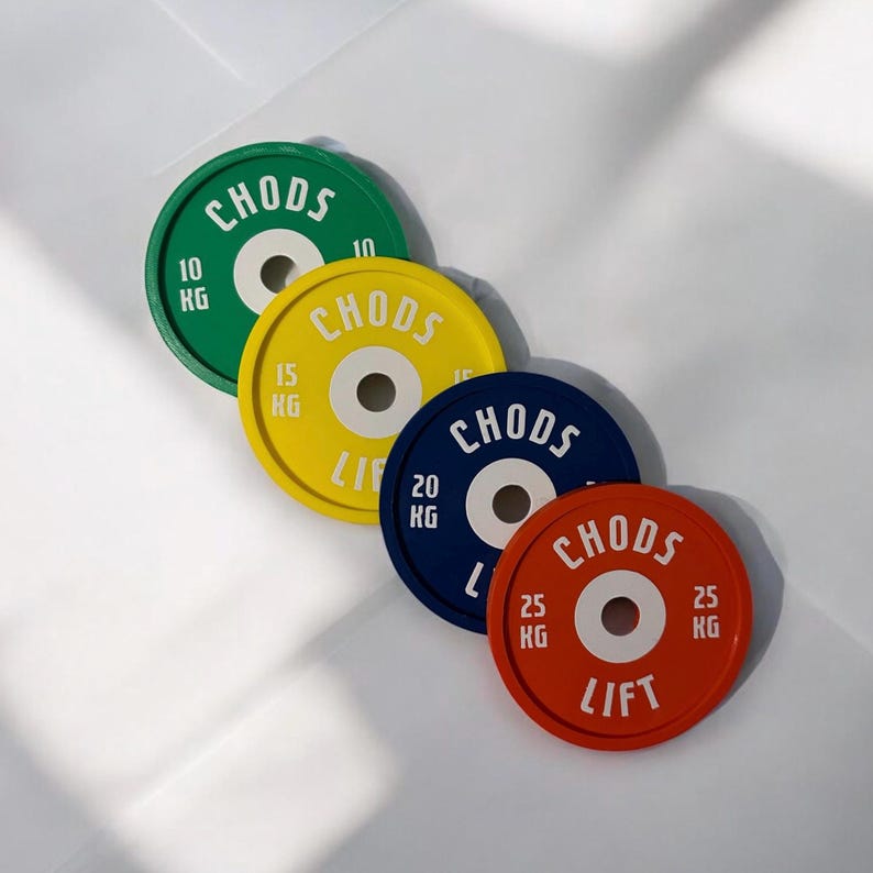 Puede incluir: Cuatro discos de pesas circulares en verde, amarillo, azul y rojo, cada uno con un orificio central blanco y texto blanco que dice CHODS LIFT. Los discos est&aacute;n etiquetados con pesos de 10 kg, 15 kg, 20 kg y 25 kg, dispuestos en fila diagonal.