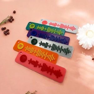 Op de afbeelding: Een set van zes kleurrijke sleutelhangers met een Spotify-barcode ontwerp. De sleutelhangers zijn in tinten rood, oranje, geel, groen, paars en zilver.