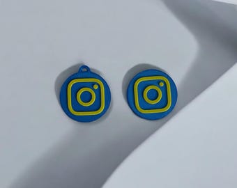 May include: Two blue and yellow Instagram logo charms. The charms are round and have a raised design.