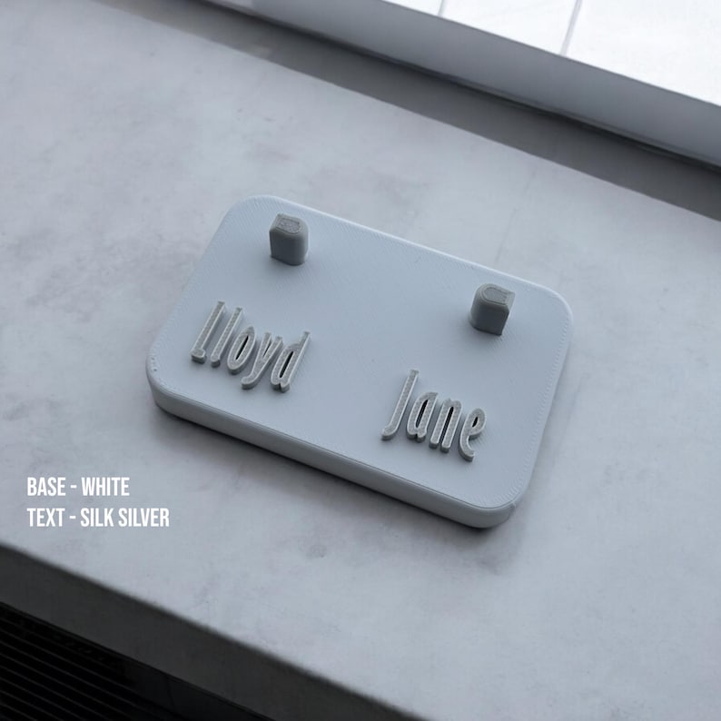 May include: White rectangular nameplate with the names "Lloyd" and "Jane" printed in silver lettering. Two small silver squares are attached to the nameplate.