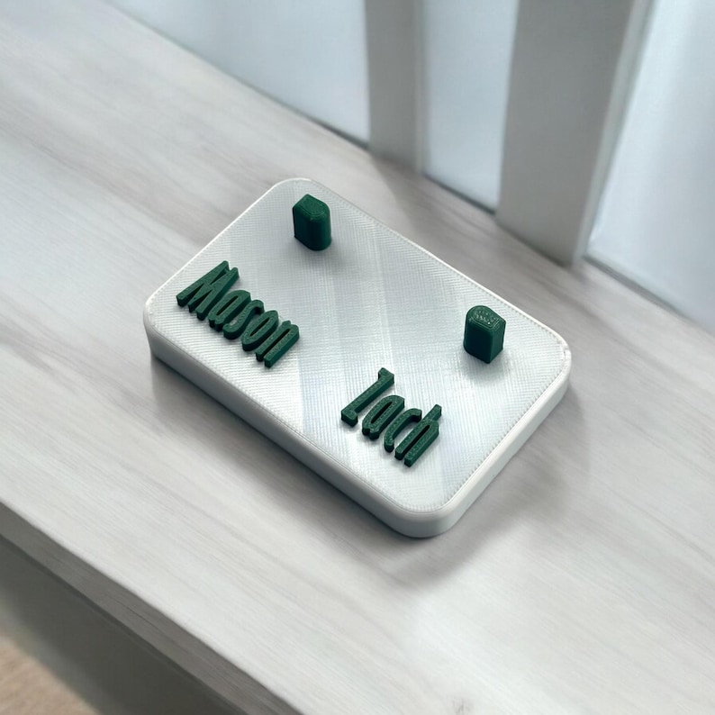 May include: White rectangular sign with the names "Mason" and "Jack" printed in green. Two small green blocks are placed on the sign.