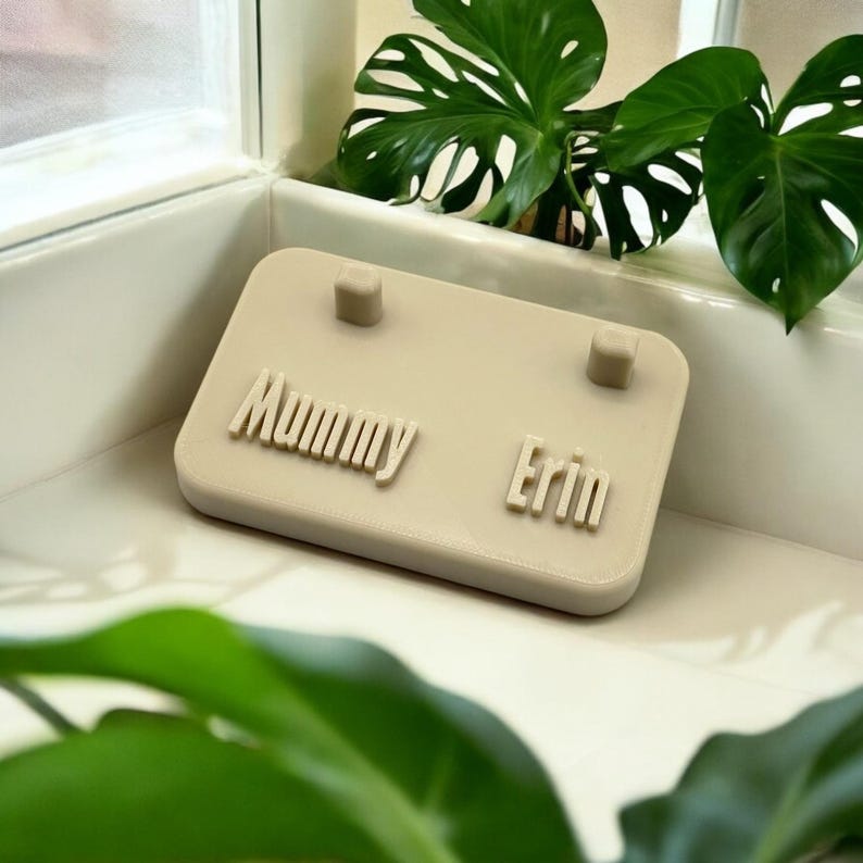 May include: A beige plastic jewelry stand with two slots for rings or earrings. The stand has the names "Mummy" and "Erin" printed on it.