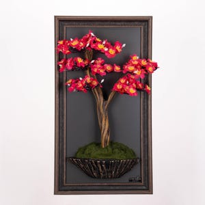 Peut inclure: Une œuvre d'art encadrée représentant un bonsaï avec des fleurs rouges et jaunes. L'arbre a un tronc brun et est placé dans un pot foncé et texturé rempli de mousse verte, sur fond gris foncé.