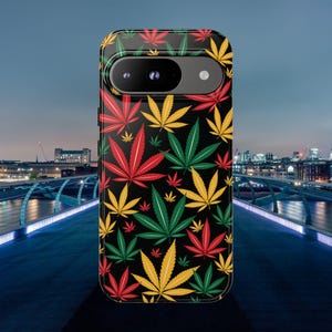 Puede incluir: Funda de teléfono negra con un patrón repetido de hojas de cannabis rojas, amarillas y verdes. La funda tiene un recorte para la cámara y un diseño moderno, ideal para proteger tu teléfono.