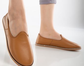May include: A pair of brown leather slip-on shoes with a pointed toe and a white stitching detail around the sole.