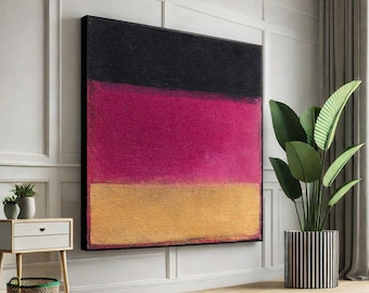 May include: Large abstract painting with a black top section, a vibrant magenta middle, and a golden yellow bottom. The artwork is framed in black and hangs on a white wall. A potted plant with large green leaves sits nearby.