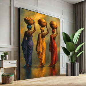 Puede incluir: Una gran pintura enmarcada representa a tres mujeres con túnicas fluidas, cada una llevando una cesta sobre la cabeza. Las mujeres visten tonos de azul, amarillo y rojo. La pintura tiene una paleta de colores cálidos y dorados y se exhibe en una habitación con una planta.