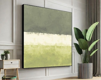 May include: Abstract art print with a black frame. The artwork features a layered design with shades of green and white. The painting is displayed in a room with a plant in a striped pot and a small side table.