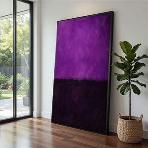 May include: Large abstract painting with a black frame. The artwork features a gradient of purple hues at the top and a dark purple-black color at the bottom. A potted plant in a woven basket sits nearby, adding a touch of nature to the room.