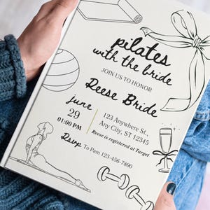 May include: A white invitation with black line art and text that reads "pilates with the bride." The invitation includes the date, time, location, and RSVP information. The invitation is held by a person.