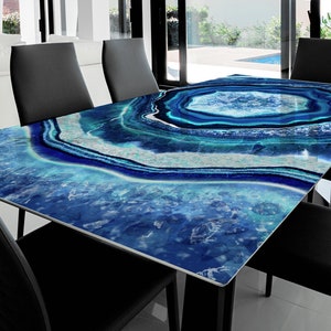 Può includere: Un tavolo da pranzo moderno con un piano in vetro con motivo di agata blu. Il tavolo è circondato da sedie nere.