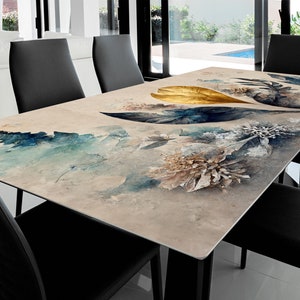 May include: A beige rectangular dining table with a black metal base. The table top features a watercolor design of blue, gold, and white leaves and flowers.