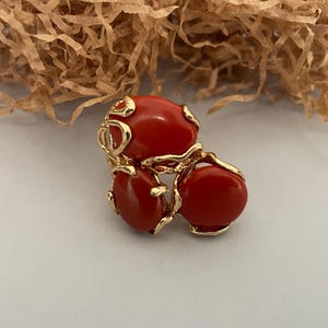 May include: A gold ring with three red oval-shaped stones set in a swirling design.