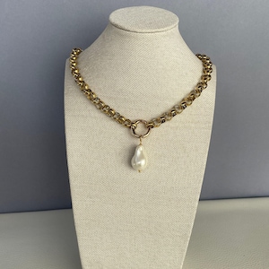 May include: A gold chain necklace with a large, white pearl pendant. The chain is made of small, linked circles.