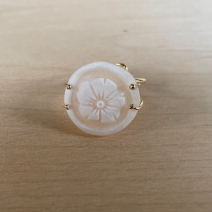 May include: A white oval ring with a carved flower design and a gold metal band.