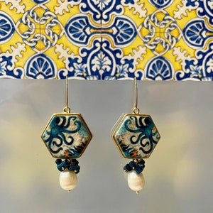 Könnte beinhalten: Goldene sechseckige Ohrringe mit einem blauen und weißen Kraken-Design und einem weißen Perlen-Anhänger.