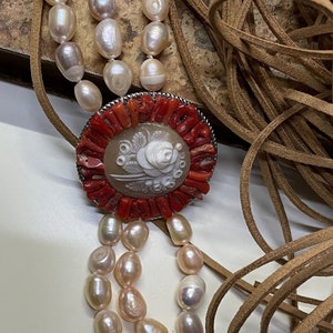 May include: A double strand pearl bracelet with a cameo pendant. The cameo features a white rose carved into a shell and is surrounded by red coral. The bracelet has silver clasps.