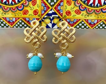 May include: Gold knot earrings with turquoise and pearl accents. The earrings are dangling and have a delicate design.