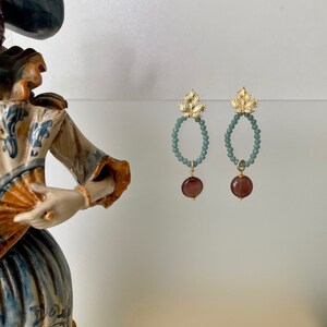Puede incluir: Un par de pendientes de hoja de oro con un óvalo de cuentas azul turquesa y un colgante de piedra púrpura oscura.