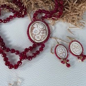 May include: A red gemstone necklace with a white cameo pendant featuring a floral design. The necklace is paired with matching earrings with white cameo floral designs.