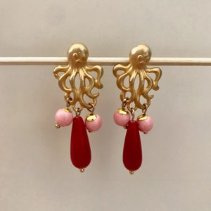 Könnte beinhalten: Goldene Ohrringe mit Tintenfisch-Anhängern und rosa und roten Glasperlen.