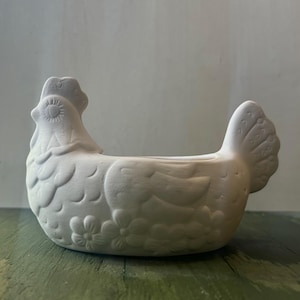 Puede incluir: Maceta de cerámica blanca en forma de gallina con diseño floral. La maceta tiene forma de gallina con la cola levantada y una pequeña abertura para plantar.