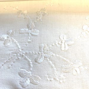 May include: White fabric with delicate embroidered floral designs. The embroidery is in a vine pattern with small flowers.