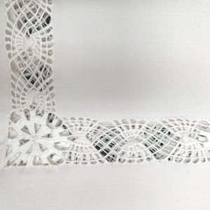 May include: White linen tablecloth with a delicate lace border. The lace features a repeating pattern of small flowers and swirls.