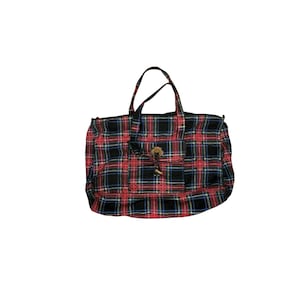 May include: A plaid tote bag in red, black, blue, and yellow. The bag has two handles and a front pocket with a wooden toggle closure. The bag is made of a woven fabric.