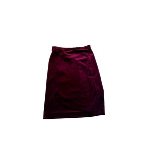 May include: A burgundy velvet skirt. The skirt is knee-length and has a wrap-style design. The fabric has a soft, luxurious appearance. The skirt is a solid color and appears to be in good condition.