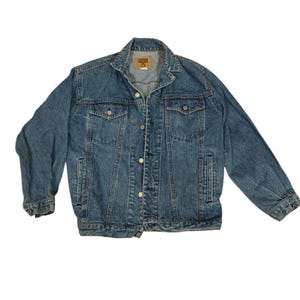 May include: A medium-wash blue denim jacket featuring a classic collar, long sleeves with buttoned cuffs, and a front button closure. The garment includes two chest pockets with buttoned flaps and two side pockets, with a tan brand label at the neck.