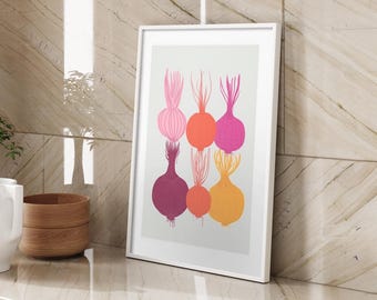 Op de afbeelding: Een ingelijste kunstprint met een kleurrijke illustratie van uien. De uien zijn afgebeeld in tinten roze, oranje en geel tegen een lichte achtergrond. De print wordt gepresenteerd in een witte lijst, wat een moderne touch geeft.