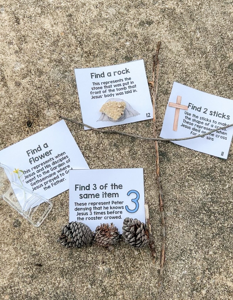 May include: Three white cards with black text on a brown, sandy surface. The cards are part of an Easter scavenger hunt. The cards read: "Find a flower", "Find a rock", and "Find 3 of the same item".
