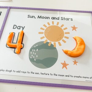 May include: A white card with the words "Day 4" in orange play dough. The card also has a picture of the sun, moon, and stars. The text "Sun, Moon and Stars" is at the top of the card. The text "play dough to add rays to the sun, texture to the moon and to create more stars" is at the bottom of the card.