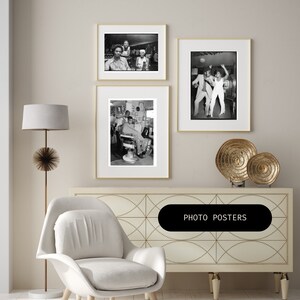 May include: Three black and white framed photographs of people in various settings. The photos are hanging on a white wall above a white dresser with a geometric pattern. The dresser has a gold metal decorative stand with a round top and three legs. The stand is holding two gold metal decorative plates. The dresser is also topped with a white armchair. The text "PHOTO POSTERS" is printed on a black rectangle in the center of the dresser.