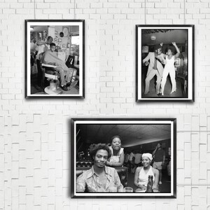May include: Three black and white framed photographs on a white brick wall. The first photo shows a man getting a haircut in a barbershop. The second photo shows two people dancing in a nightclub. The third photo shows three people sitting at a table in a restaurant.