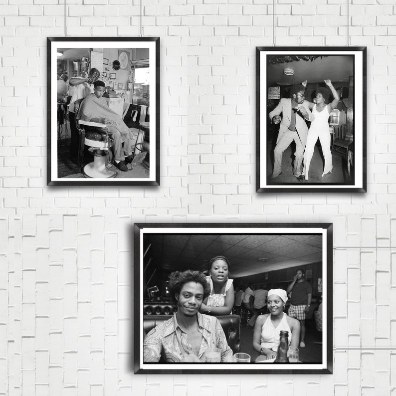 May include: Three black and white framed photographs on a white brick wall. The first photo shows a man getting a haircut in a barbershop. The second photo shows two people dancing in a nightclub. The third photo shows three people sitting at a table in a restaurant.