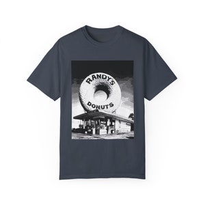 Puede incluir: Una foto en blanco y negro de una tienda de donas con una dona gigante sobre el edificio. La tienda se llama "Randy's Donuts".