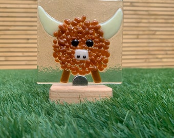 Può includere: Ornamento in vetro raffigurante una mucca delle Highlands. Il pannello di vetro quadrato ha uno sfondo strutturato e presenta una mucca con un corpo marrone strutturato, occhi neri e corna color crema. Montato su una piccola base di legno.