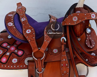 May include: Brown leather saddle with pink and white floral embroidery and a silver cross design. The saddle is decorated with silver studs and comes with a matching bridle.
