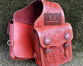 May include: A brown leather saddle bag with intricate floral tooling and silver accents. The bag has two compartments and a flap closure.