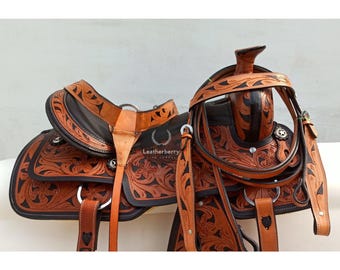 May include: A brown leather saddle with intricate floral tooling and black accents. The saddle is paired with a matching leather bridle with silver hardware.