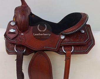 May include: A brown leather saddle with black suede seat and silver accents. The saddle features intricate tooling and a "Leatherberry Live Luxury" logo.