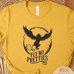May include: Mustard yellow t-shirt with a black graphic of a winged monkey inside a circle, with the text "FLY MY PRETTIES". The shirt is made of Bella Canvas material.