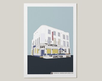 May include: A white building with a blue awning and the text "The Junction" in red letters. The building has a cafe sign with the text "Cafe" in yellow letters. The building is on a street corner and has a blue sky in the background.